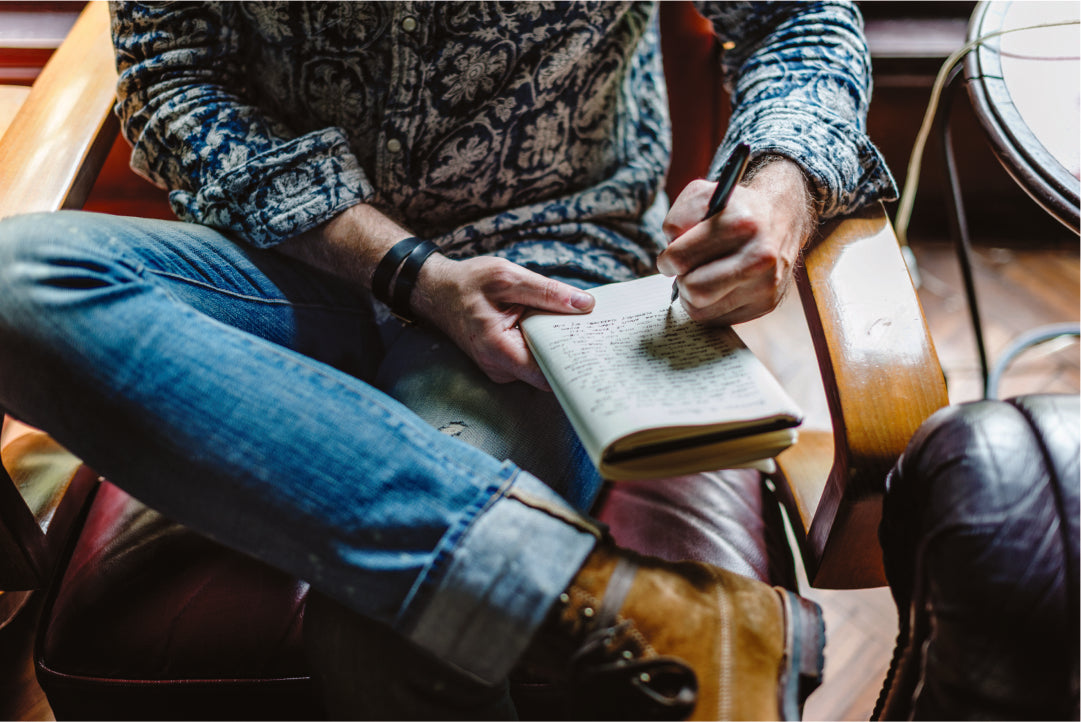 Person sitting on a chair, writing in a notebook wearing leather boots