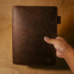 Hand holding a dark brown leather notebook cover against a beige background