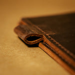 Close-up of a dark brown leather journal cover with pen holder on a matching brown background