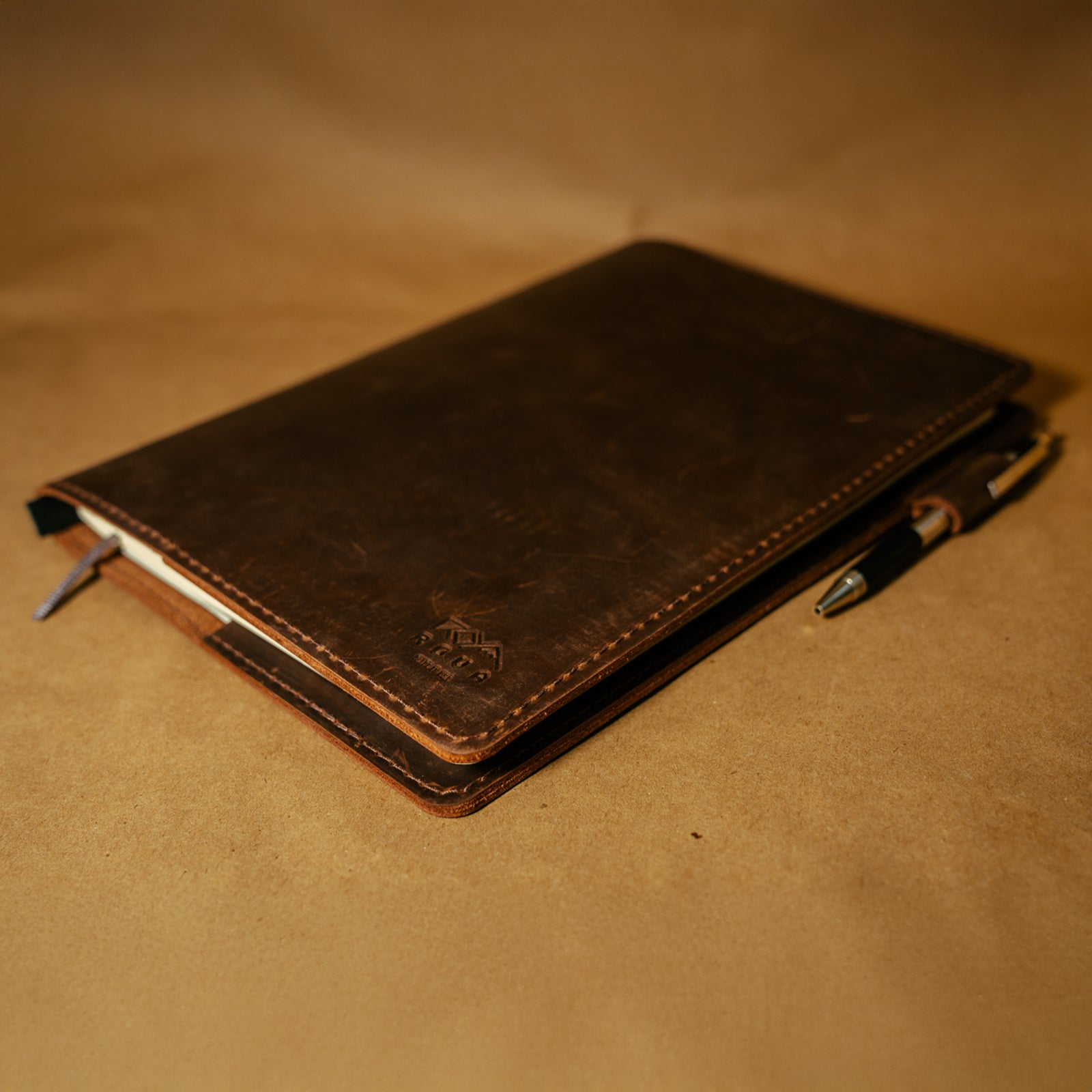 Dark Brown leather notebook journal cover with pen on a matching brown background