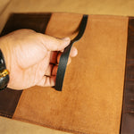 Hand holding a black leather bookmark over a brown leather notebook cover
