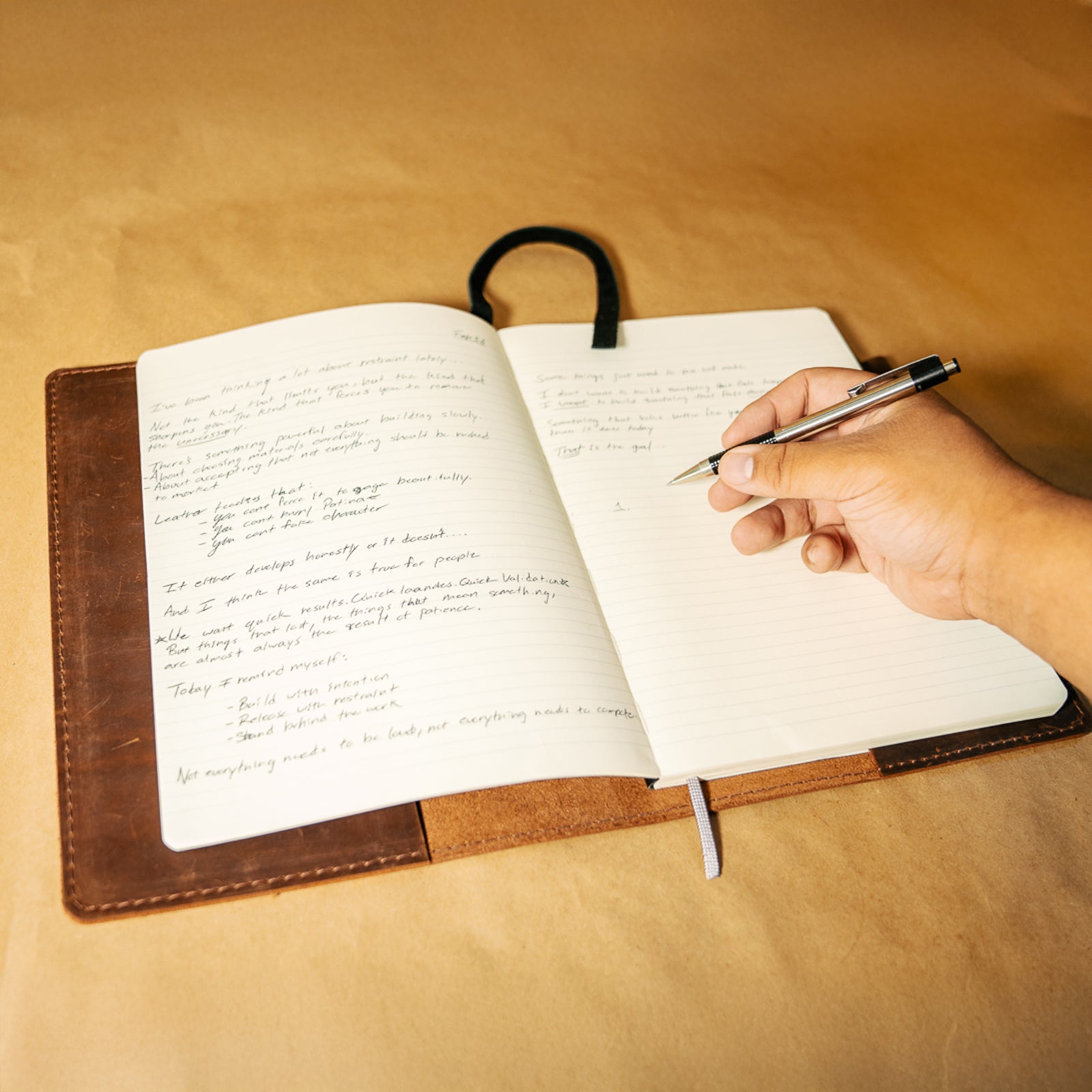 Hand writing in a Moleskine notebook with a leather cover on a beige background