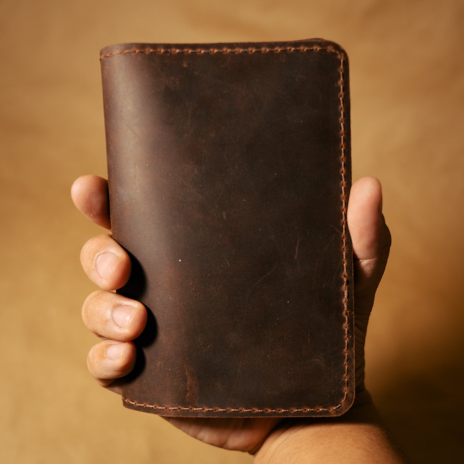 Hand holding a brown leather field notes cover against a matching background