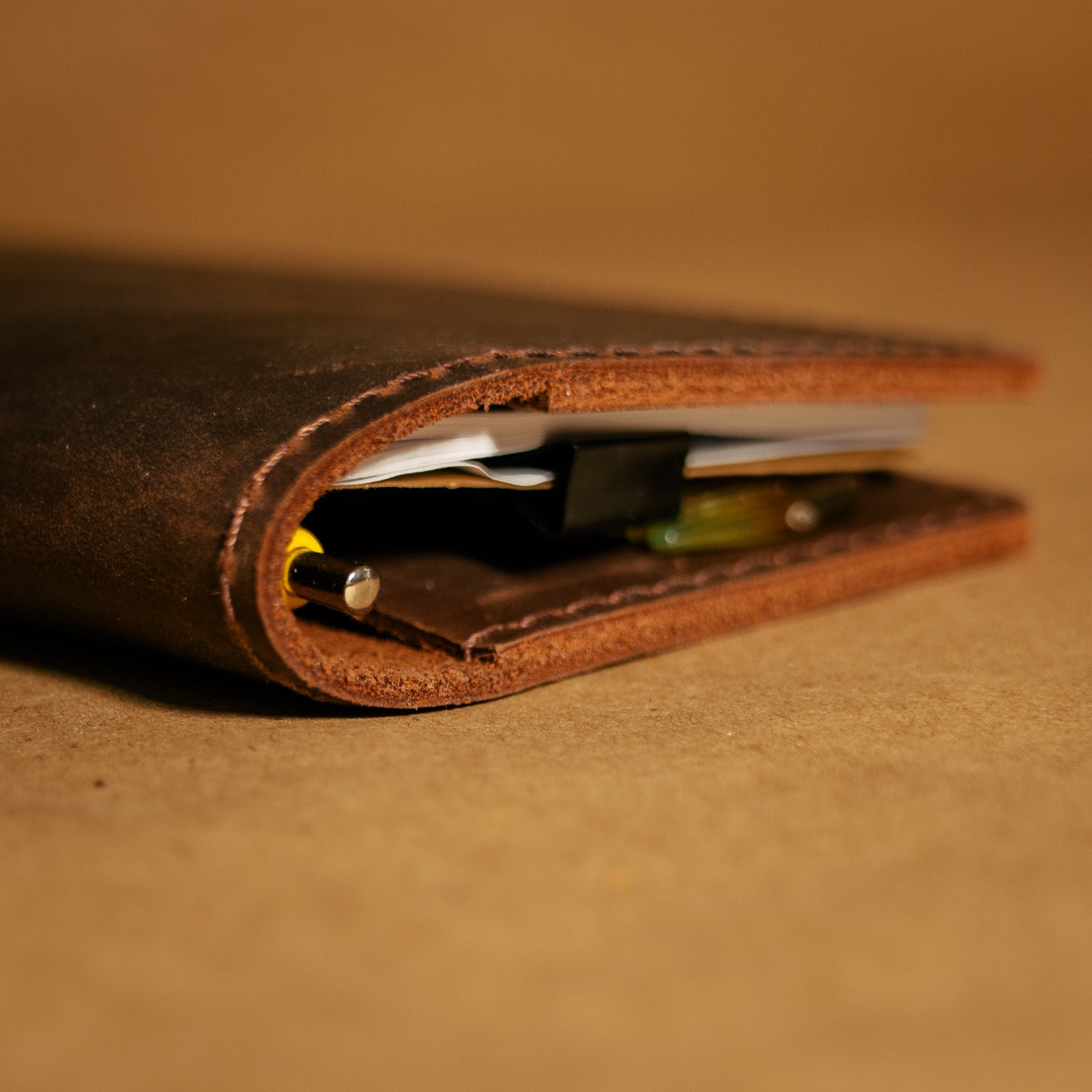 Close up of a brown leather field notes cover with money and cards on a matching brown background