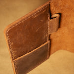 Close-up of a brown leather field notes cover showing pen loop and card holder on a beige background