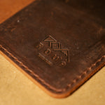 Close up of a brown leather field notes cover with an embossed logo on a wooden surface