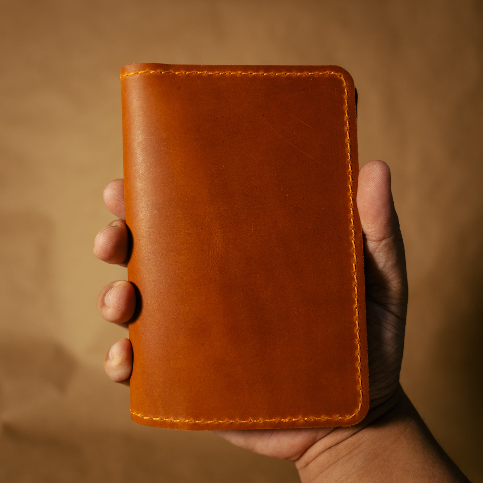 Hand holding a whiskey orange leather field notes journal cover against a beige background