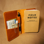 Whiskey orange leather field notes journal cover with a 'Field Notes' notebook and pen on a brown background