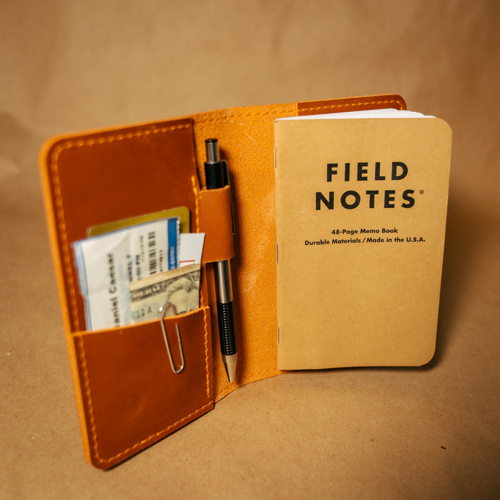 Whiskey orange leather field notes journal cover with a 'Field Notes' notebook and pen on a brown background