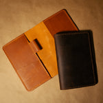 Two leather field notes journal covers, one dark brown and one whiskey orange, on a beige background