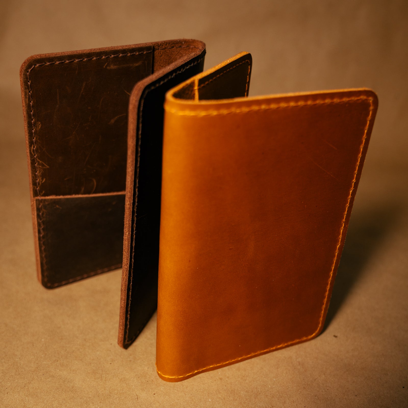 Two leather  leather field notes cover, one dark brown and one whiskey orange, on a brown background