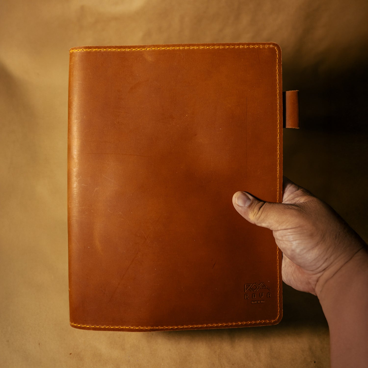 Whiskey Orange leather notebook cover held by a hand against a beige background