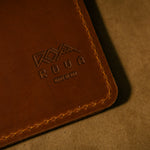 Dark Brown leather notebook cover with embossed logo and stitching on a matching brown background
