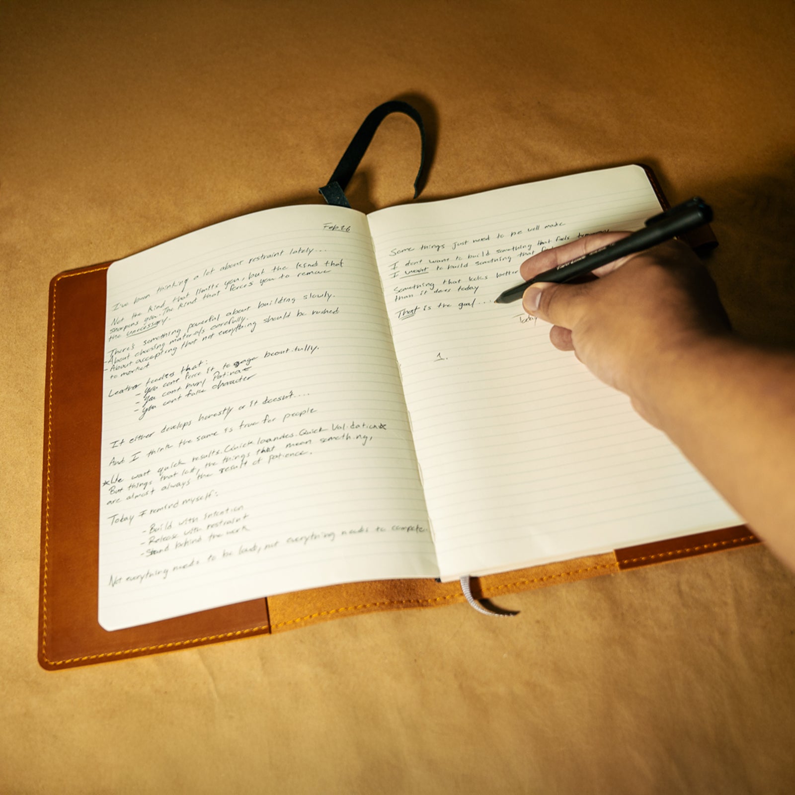 Handwriting in a Moleskine notebook with leather cover and a hand holding a pen on a wooden surface
