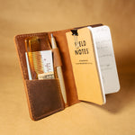 Brown field notes cover with field notes notebook, pen, and comb on a brown background
