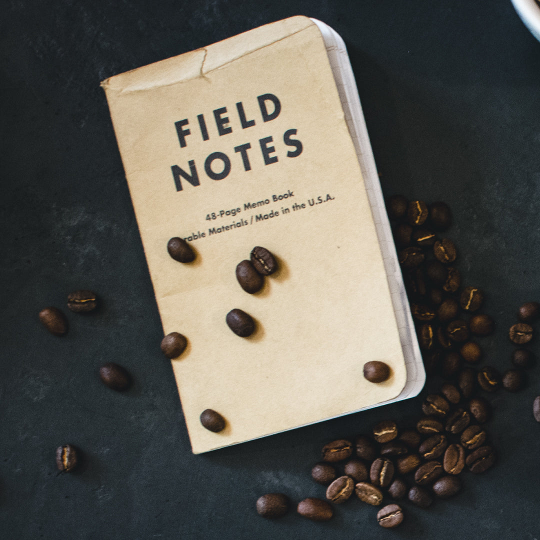 Field Notes notebook with coffee beans on a dark surface