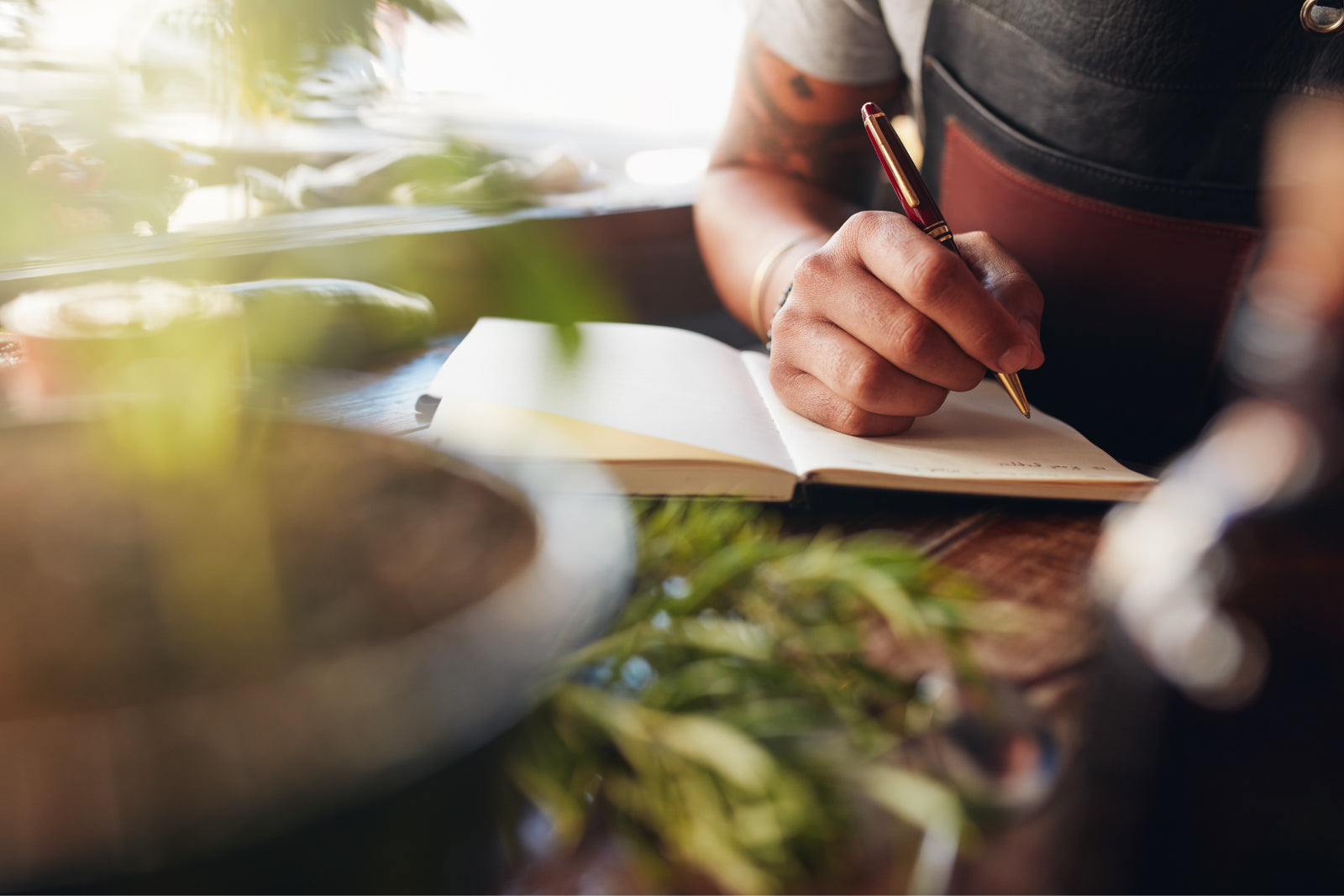 Person writing in an A5 notebook with a pen, surrounded by greenery